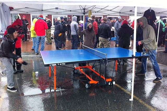 People playing on an early Tiger table in the rain beneath a white event tent.